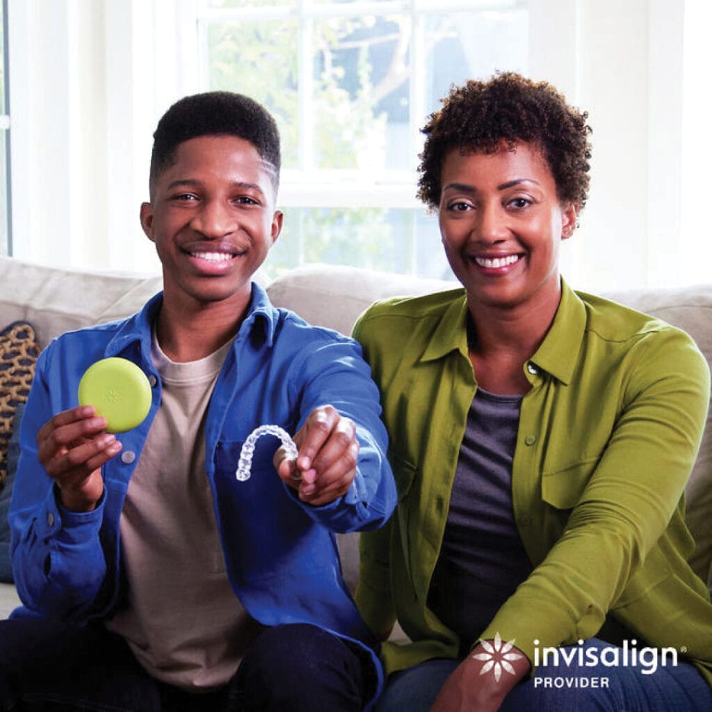 A smiling man holds a green Invisalign case and aligner tray while sitting next to a smiling woman on a couch in Round Rock; perfect smiles for teens and adults. Invisalign Provider logo in corner.