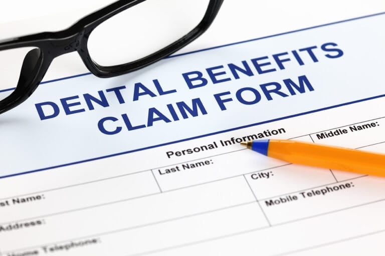 A close-up of a dental benefits claim form with a pair of glasses and an orange pen resting on it, highlighting important details for Orthodontics Financing in Round Rock.
