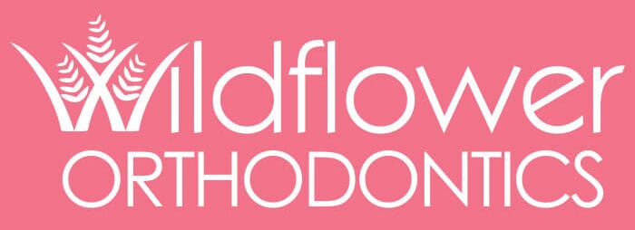 Wildflower Orthodontics logo in white text on a pink background, featuring a wildflower graphic elegantly integrated into the letter "W." Perfect for showcasing an inviting and modern orthodontics logo.