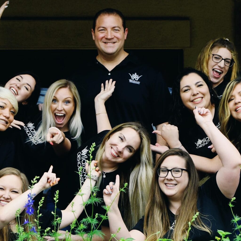 About Wildflower Orthodontics team smiling together in branded shirts with greenery in the foreground.
