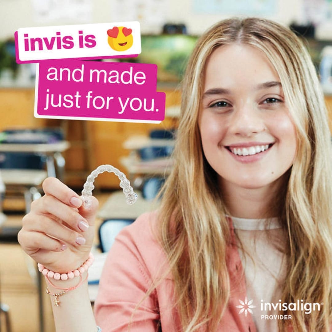 Young woman sitting in a classroom holding a clear aligner, with text saying "invis is and made just for you." Invisalign Provider logo in the corner.