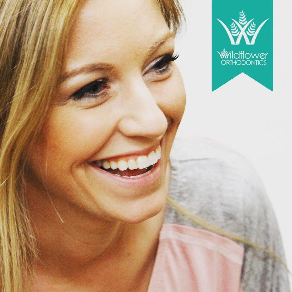 A woman smiling, showing her teeth, with the Wildflower Orthodontics logo in the top right corner.