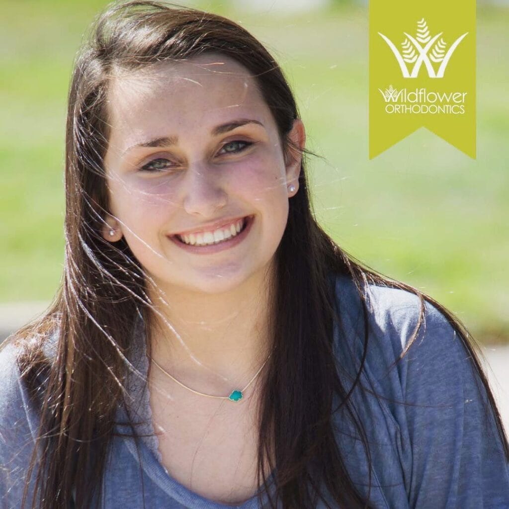 Young woman with long brown hair smiles outdoors; Wildflower Orthodontics logo is in the top right corner of the image.