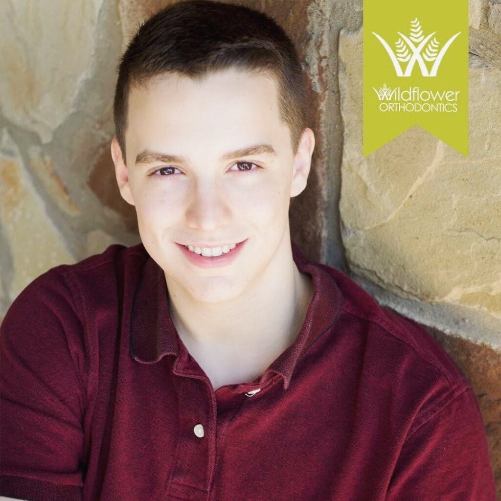 A young person with short brown hair wearing a maroon polo shirt smiles in front of a stone wall. A "Wildflower Orthodontics" logo appears in the top right corner.