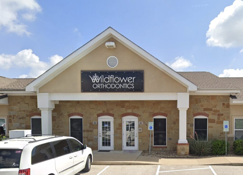 A beige, single-story building with a sign reading "Wildflower Orthodontics" above the entrance tells you all about its purpose, with a white van parked in front.
